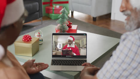 Happy-african-american-senior-couple-on-laptop-video-call-with-santa-claus-at-christmas-time