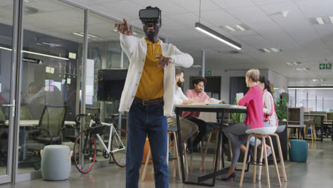 Happy-african-american-businessman-using-vr-headset-over-colleagues-in-office