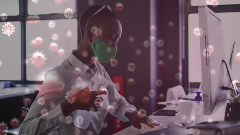 Animation-Von-Viruszellen-über-Einer-Afroamerikanischen-Geschäftsfrau-Mit-Gesichtsmaske,-Die-Im-Büro-Desinfiziert-Wird