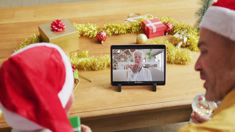 Caucasian-father-and-son-with-santa-hats-using-tablet-for-christmas-video-call-with-woman-on-screen