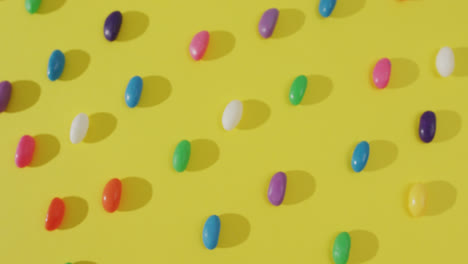 Video-of-overhead-view-of-rows-of-multi-coloured-sweets-over-yellow-background