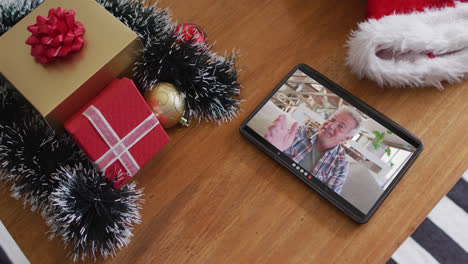 Smiling-senior-caucasian-man-talking-on-christmas-video-call-on-tablet