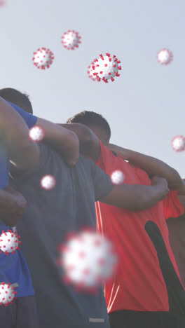 Animation-of-virus-cells-floating-over-diverse-group-of-male-football-players-embracing