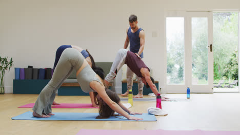 Diverse-group-practicing-yoga-pose-in-class-with-male-instructor-helping