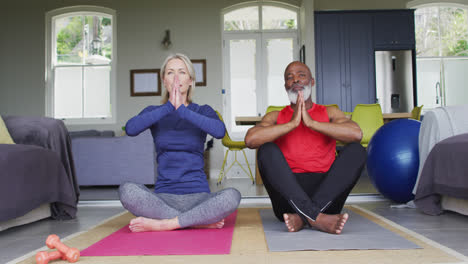 Mixed-race-senior-couple-practicing-yoga-together-at-home