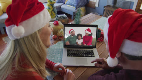 Caucasian-couple-with-santa-hats-using-laptop-for-christmas-video-call-with-family-on-screen