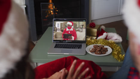 Rear-view-of-caucasian-couple-wearing-santa-hats-having-a-videocall-on-laptop-during-christmas