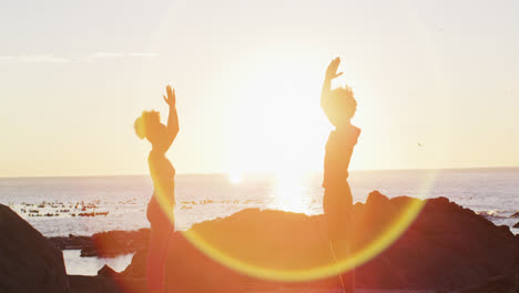Afroamerikanisches-Paar,-Das-Bei-Sonnenuntergang-Gemeinsam-Yoga-Auf-Den-Felsen-In-Der-Nähe-Des-Meeres-Praktiziert