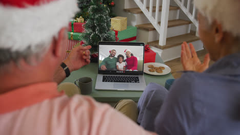 Happy-caucasian-senior-couple-on-laptop-video-call-with-family-at-christmas-time