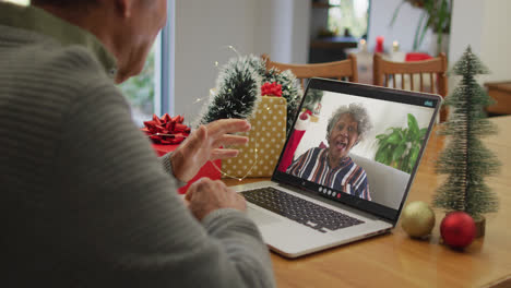 Caucasian-senior-man-having-christmas-video-call-on-laptop-with-african-american-senior-woman