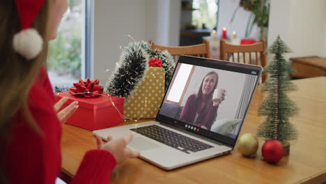 Caucasian-woman-on-laptop-video-call-with-happy-female-friend-at-christmas-time
