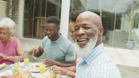 Portrait-of-happy-african-american-family-talking-and-having-breakfast-in-garden
