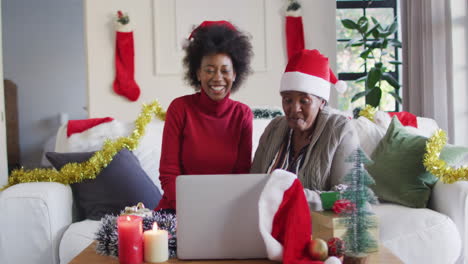 Happy-african-american-mother-and-adult-daughter-in-santa-hats-on-christmas-video-call,-slow-motion