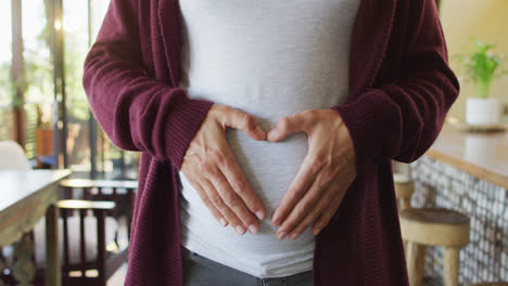 Midsection-of-caucasian-pregnant-woman-gesturing-heart-over-belly