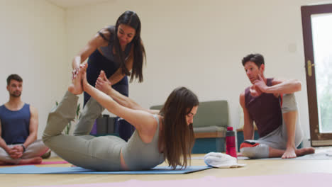 Diverse-group-practicing-yoga-in-class-with-smiling-female-instructor-helping