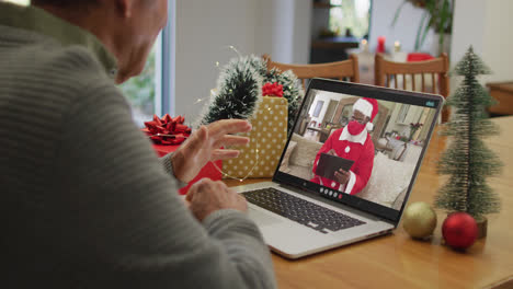 Kaukasischer-älterer-Mann,-Der-Einen-Weihnachtsvideoanruf-Auf-Dem-Laptop-Mit-Einem-Afroamerikanischen-Weihnachtsmann-In-Einer-Gesichtsmaske-Führt