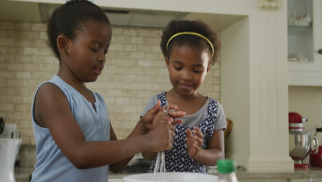 Happy-two-african-american-girls-baking-and-mixing-ingredients-in-kitchen