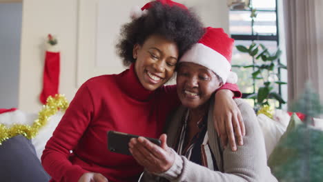 Happy-african-american-mother-and-adult-daughter-in-christmas-hats-using-smartphone,-slow-motion