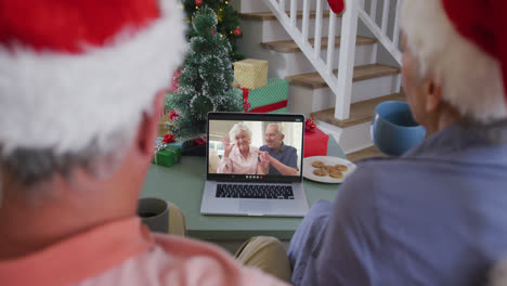 Happy-caucasian-senior-couple-on-laptop-video-call-with-senior-couple-at-christmas-time