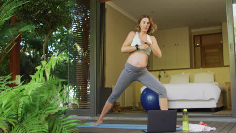 Caucasian-pregnant-woman-practicing-yoga-at-home-with-online-lessons
