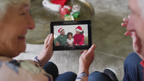 Senior-caucasian-couple-using-tablet-for-christmas-video-call-with-happy-family-on-screen