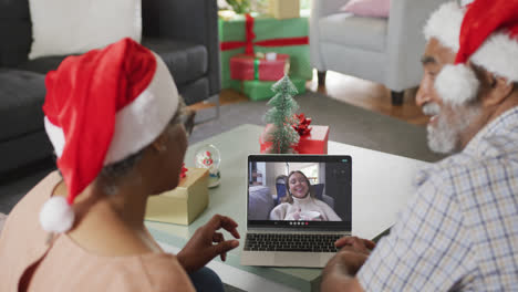 Happy-african-american-senior-couple-on-laptop-video-call-with-female-friend-at-christmas-time