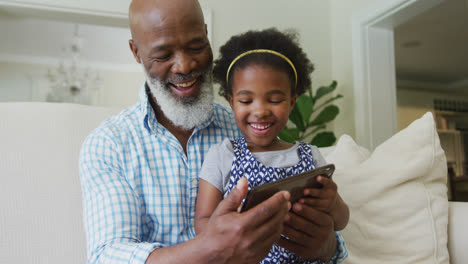 Glücklicher-Afroamerikanischer-Großvater-Mit-Enkelin,-Die-Im-Wohnzimmer-Ein-Tablet-Benutzt