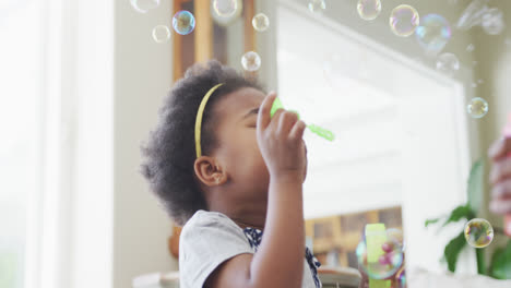 Happy-african-american-grandmother-with-granddaughter-blowing-bubbles-in-living-room
