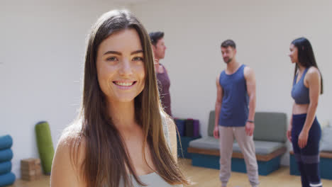 Porträt-Einer-Lächelnden-Kaukasischen-Frau-Mit-Einer-Vielfältigen-Gruppe-Im-Yoga-Kurs,-Die-Im-Hintergrund-Spricht