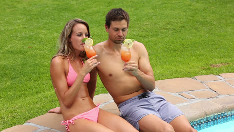 Sexy-couple-sitting-by-the-pool-on-holidays-drinking-cocktails
