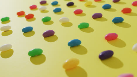Video-of-overhead-view-of-rows-of-multi-coloured-sweets-over-yellow-background