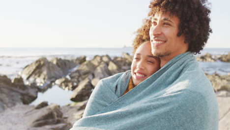 African-american-couple-wrapped-in-blanket-standing-on-the-rocks-near-the-sea