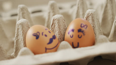 Vídeo-De-Cerca-De-Dos-Huevos-Marrones-Con-Caras-Dibujadas-En-El-Fondo-De-Un-Cartón-De-Huevos