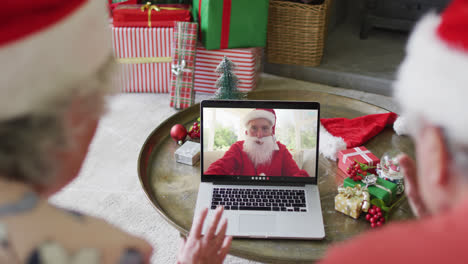 Senior-caucasian-couple-using-laptop-for-christmas-video-call-with-happy-santa-on-screen