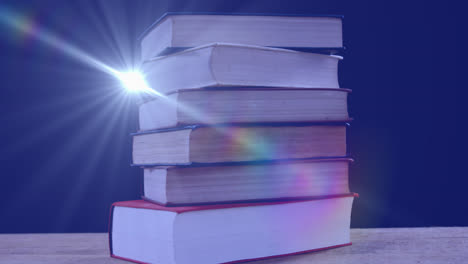 Animation-of-glowing-light-over-stack-of-books-on-blue-background