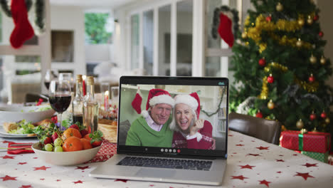 Happy-caucasian-grandparents-in-santa-hats-on-laptop-lying-on-christmas-table