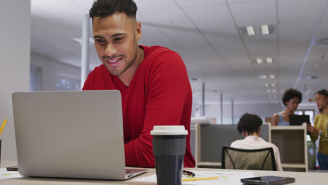 Happy-biracial-businessman-using-laptop-over-business-colleagues-in-office
