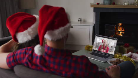 Rückansicht-Eines-Kaukasischen-Paares-Mit-Weihnachtsmützen,-Das-Während-Der-Weihnachtszeit-Einen-Videoanruf-Auf-Dem-Laptop-Führt