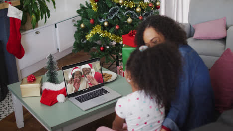 African-american-mother-and-daughter-having-a-videocall-on-laptop-at-home-during-christmas