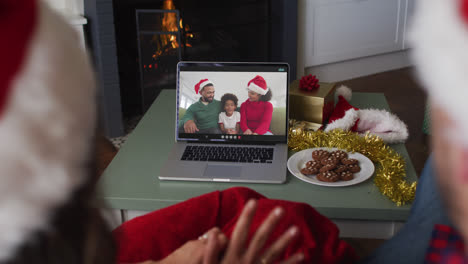 Rear-view-of-caucasian-couple-wearing-santa-hats-having-a-videocall-on-laptop-during-christmas