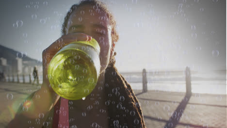 Animation-of-bubbles-over-biracial-woman-drinking-water-on-promenade
