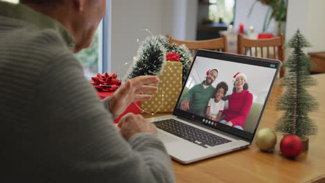 Kaukasischer-älterer-Mann,-Der-Einen-Weihnachtsvideoanruf-Auf-Dem-Laptop-Mit-Einer-Afroamerikanischen-Familie-Auf-Dem-Bildschirm-Führt