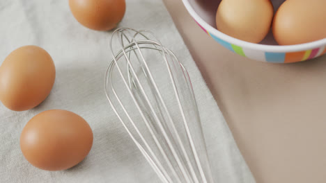 Video-of-overhead-view-of-eggs-and-egg-whisk-on-rustic-cloth-on-beige-background