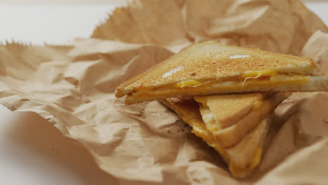 Video-of-close-up-of-toasted-cheese-sandwiches-on-brown-paper-over-grey-background