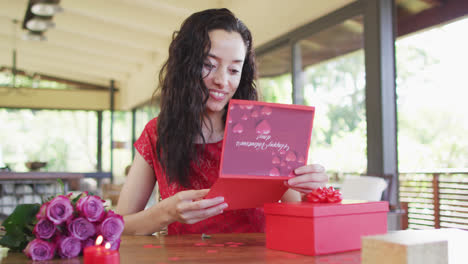 Happy-biracial-woman-opening-valentines-card-and-presents-at-home