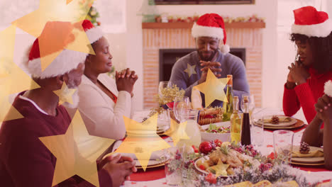 Animation-of-stars-falling-over-happy-african-american-family-wearing-santa-hats-and-praying