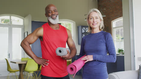 Portrait-of-mixed-race-senior-couple-holding-yoga-mat-smiling-at-home