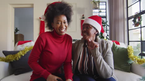 Happy-african-american-mother-and-adult-daughter-in-santa-hats-on-christmas-video-call,-slow-motion