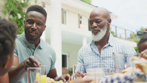 Happy-african-american-family-talking-and-having-breakfast-in-garden