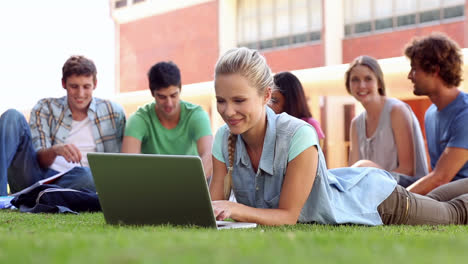 Blonde-student-using-laptop-with-classmates-sitting-behind-on-grass